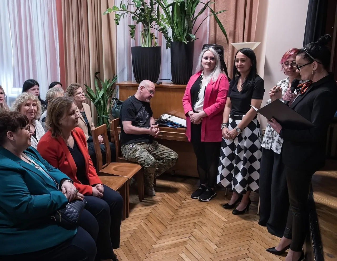 Osoby stoją przed sceną zwrócone do publiczności