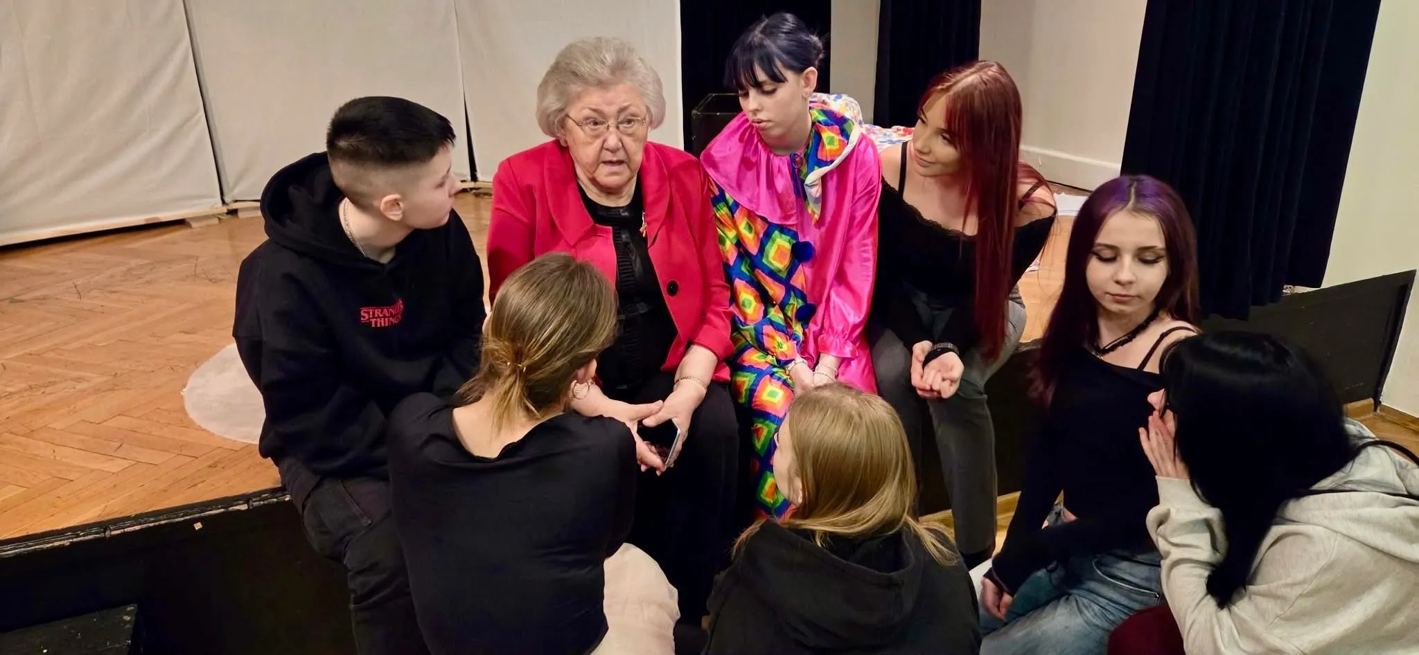 Młodzież siedzi obok starszej pani i słucha